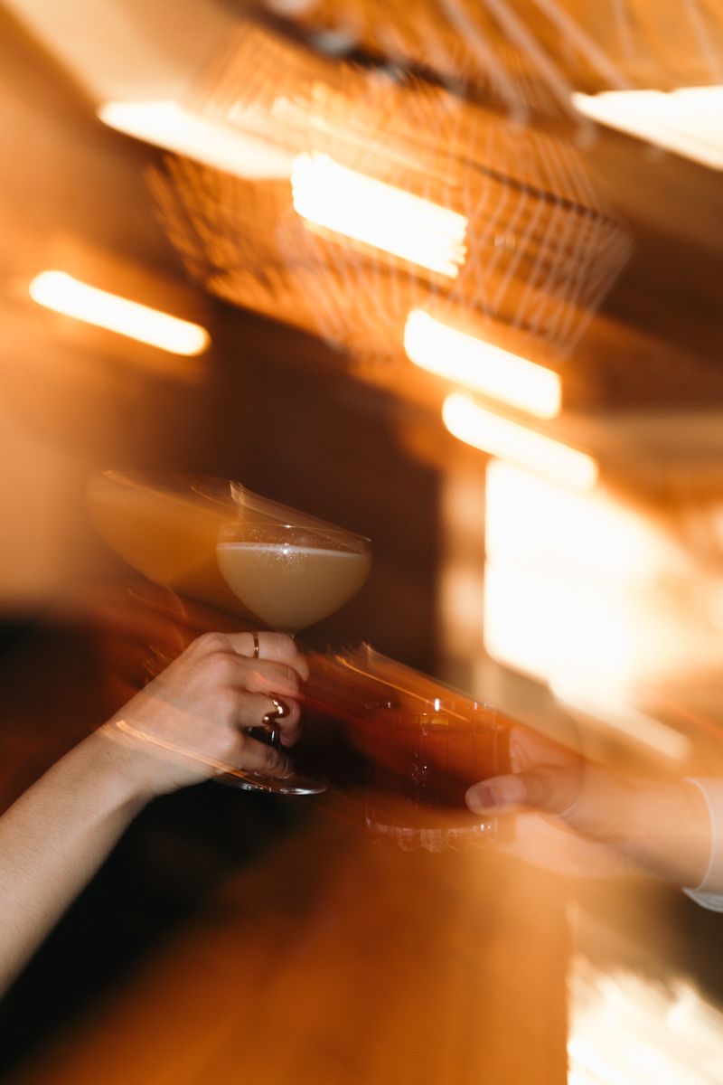 Hände mit Cocktailglas im warmen Licht der Bar