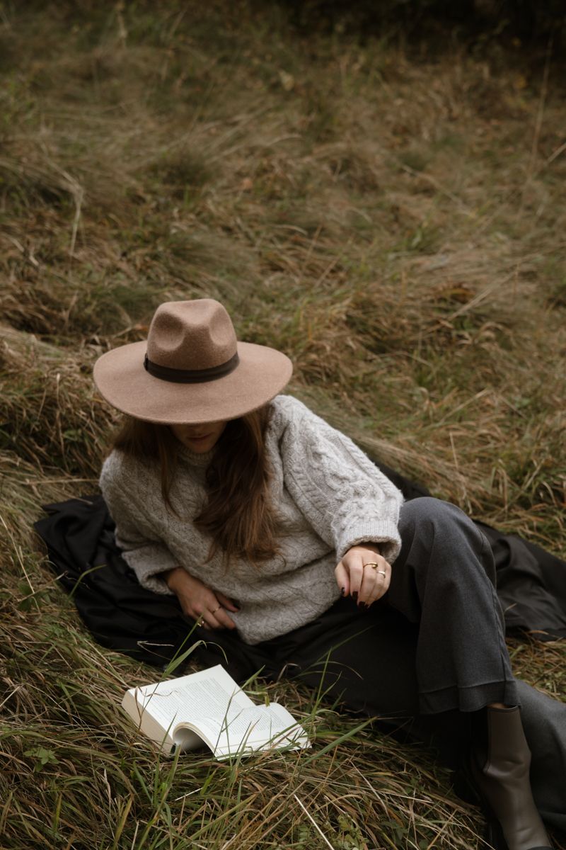 Frau liegt mit Buch und Hut im Gras