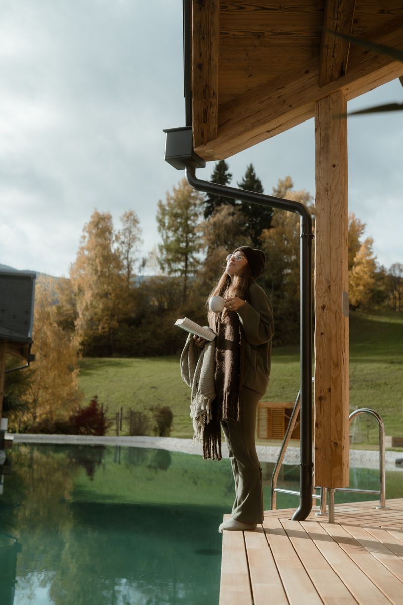 Frau am Steg der Teichlodge zwischen Herbstbäumen