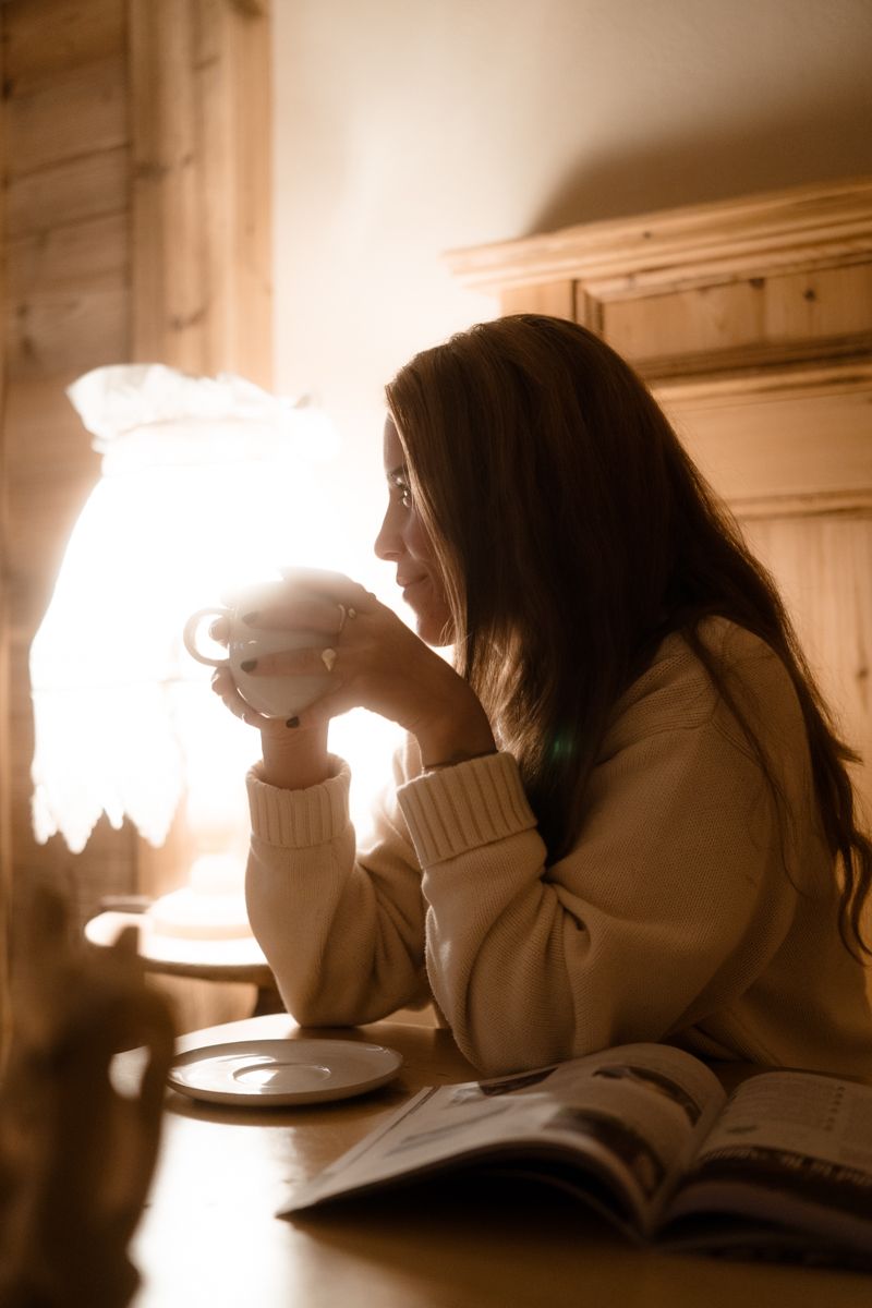 Frau mit Tasse am Holztisch im Lampenlicht