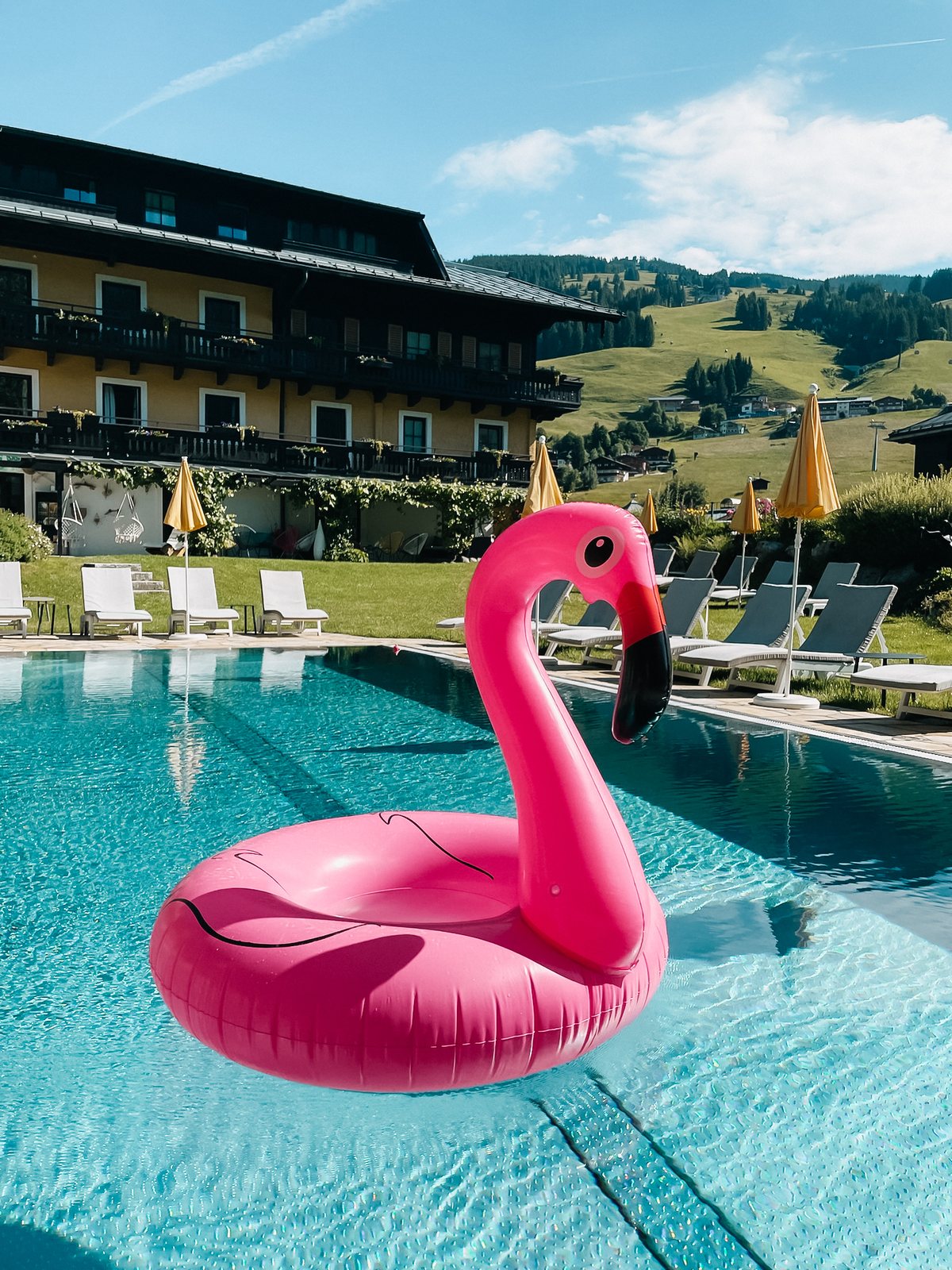 Pink-Flamingo im Außenpool des Saalbacher Hofs, gelbe Schirme und Berge